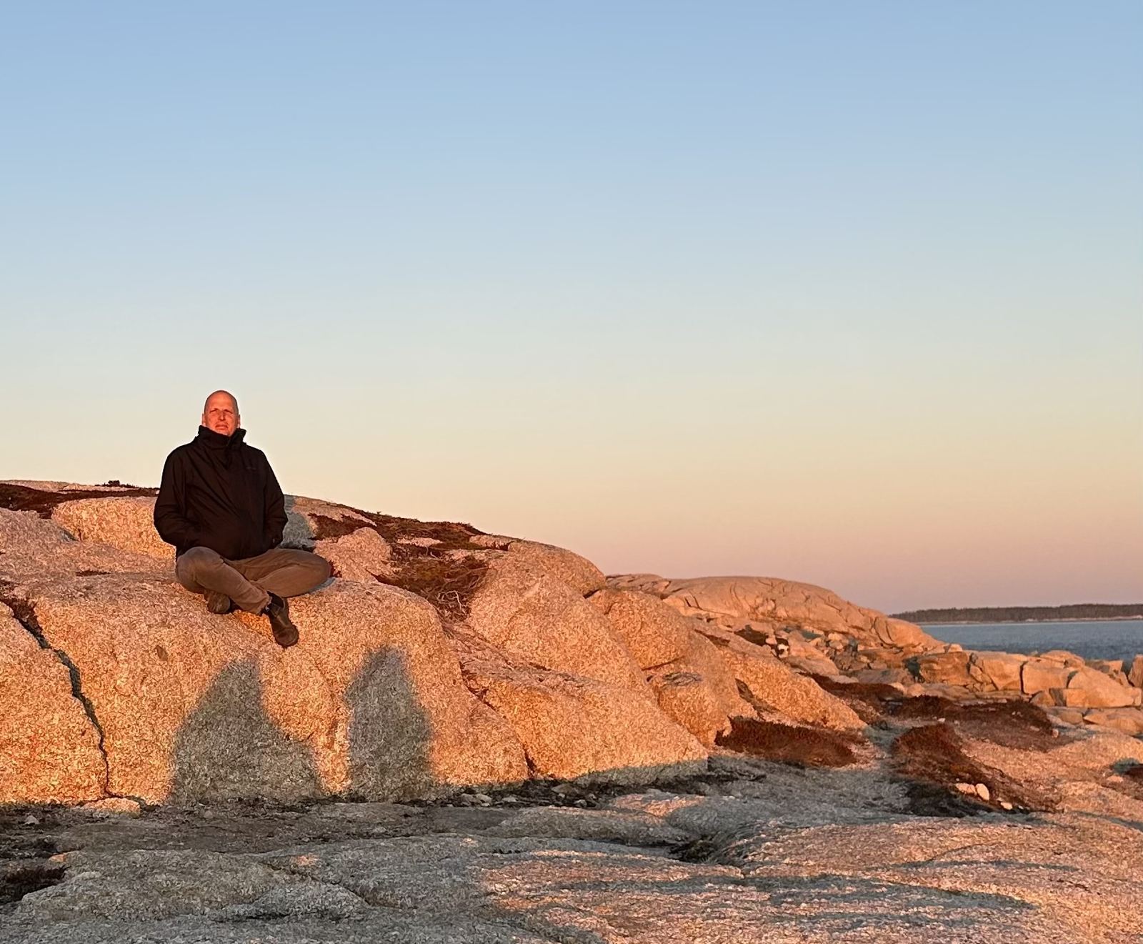Nick Matheson sitting on granite rocks by the sea at sunrise